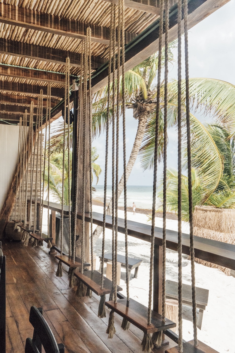 A view of the ocean and beachside with few people walking from inside a beach hut through the hanging swing set