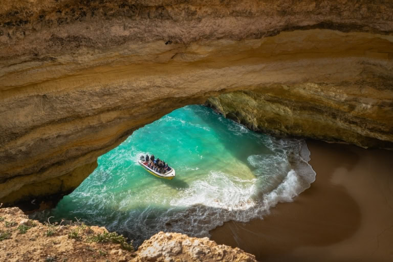 Tourists in a boat explore the turquoise waters inside the Benagil Cave in Algarve, Portugal.