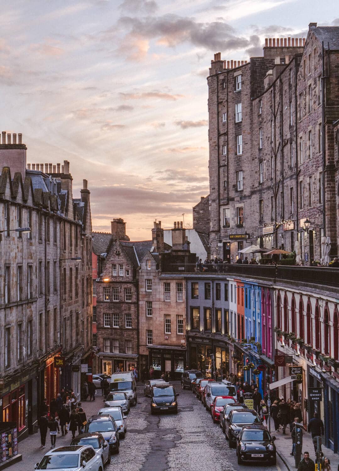 A street filled with cars and people walking surrounded by old and tall buildings in Scotland