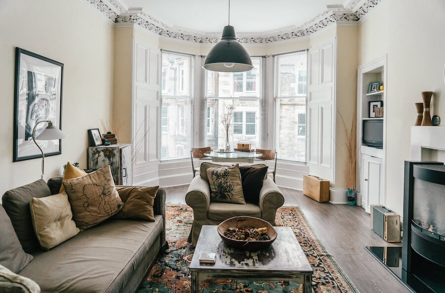 A living room with glass windows at the background, gray couches with yellow pillows, and a wooden table in the center in Old Town Edinburgh