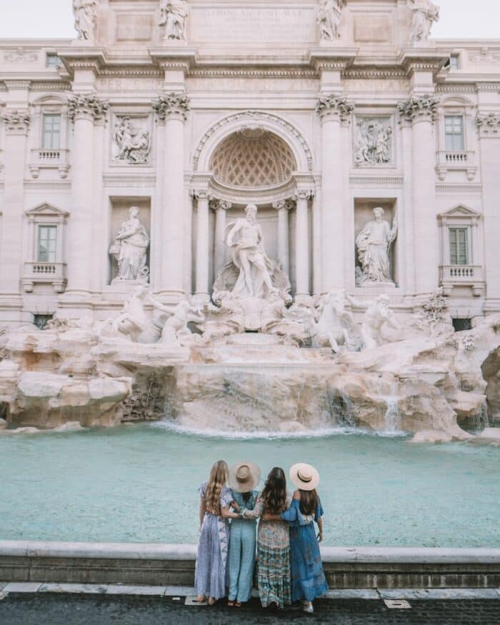 Four girls stand side by side in front of the Trevi Fountain