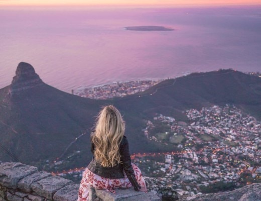 Girl sitting at the top of table mountain at sunset overlooking Cape Town, South Africa