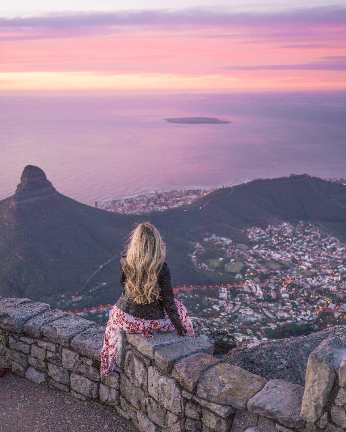 Girl sitting at the top of table mountain at sunset overlooking Cape Town, South Africa