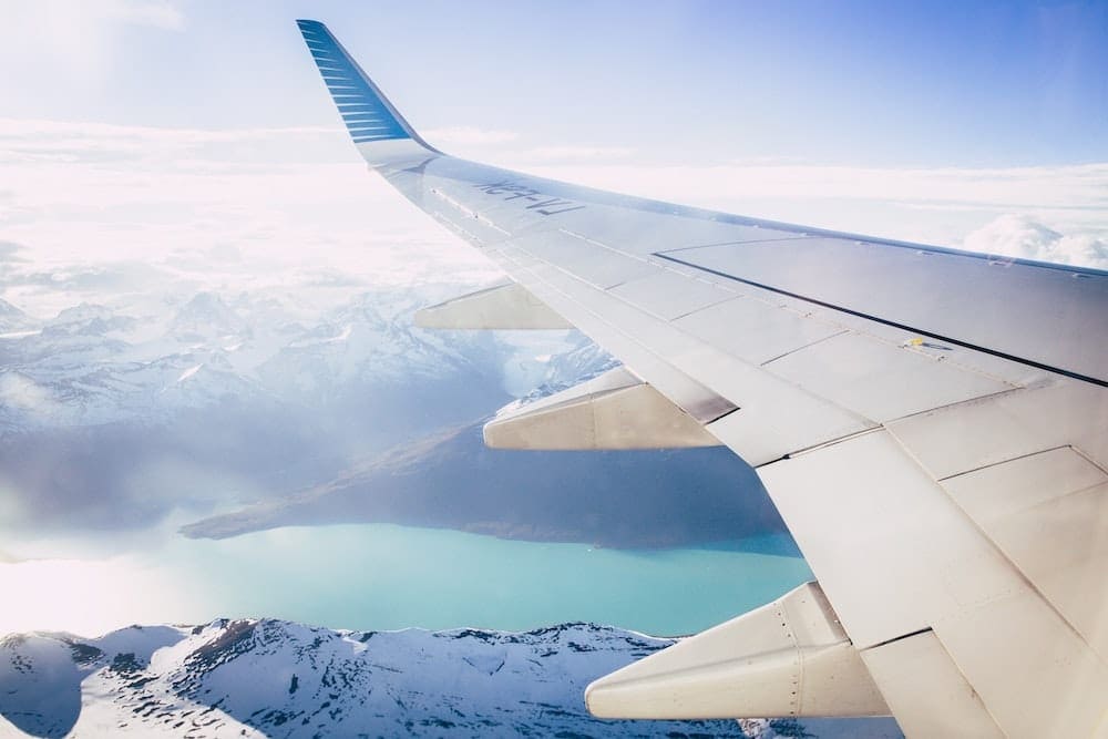 White airplane wing overlooking snowy mountain peaks