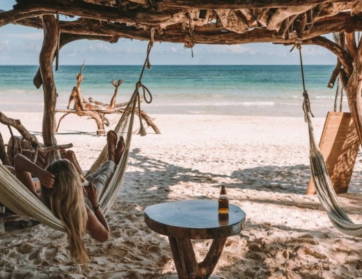 Feet resting in a hammock in front of Tulum beach with Modelo beer