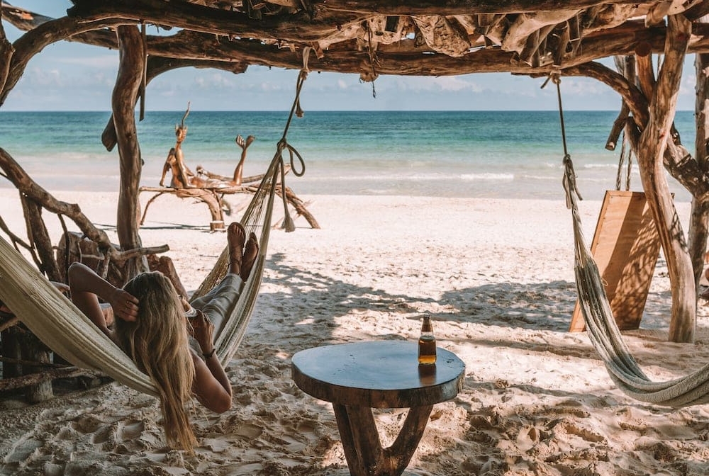 Feet resting in a hammock in front of Tulum beach with Modelo beer