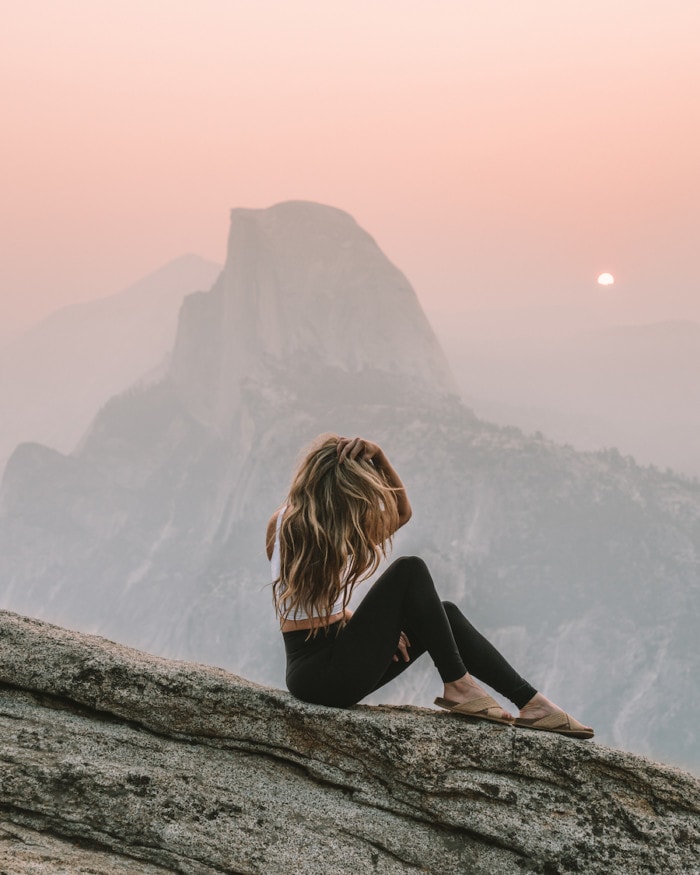 Girl sitting in front of Half Dome at Glacier Point at sunrise