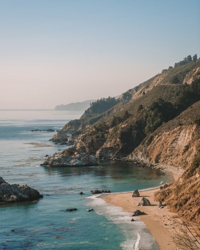 Sunny Big Sur coastline with sandy beach below dotted with unique rock formations.