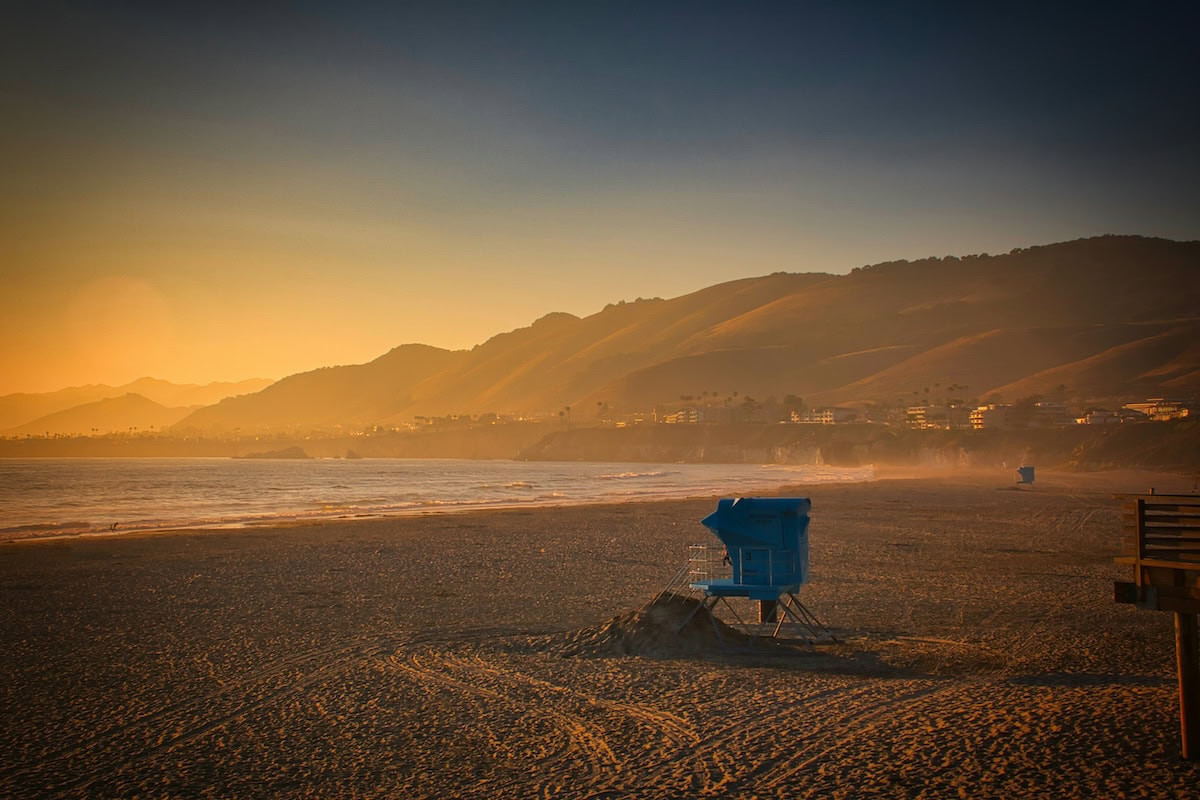 Solo lifeguard stand in the sand overlooking the beach at sunset.