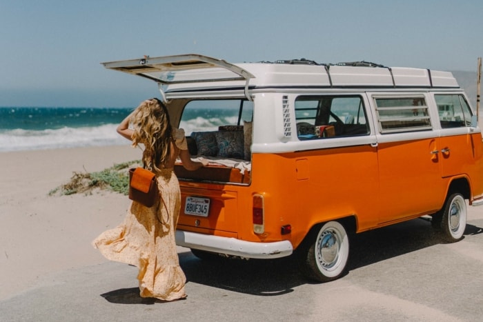 Michelle Halpern standing next to a vintage orange campervan by the beach