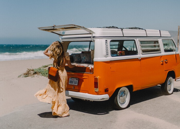 Michelle Halpern standing next to a vintage orange campervan by the beach