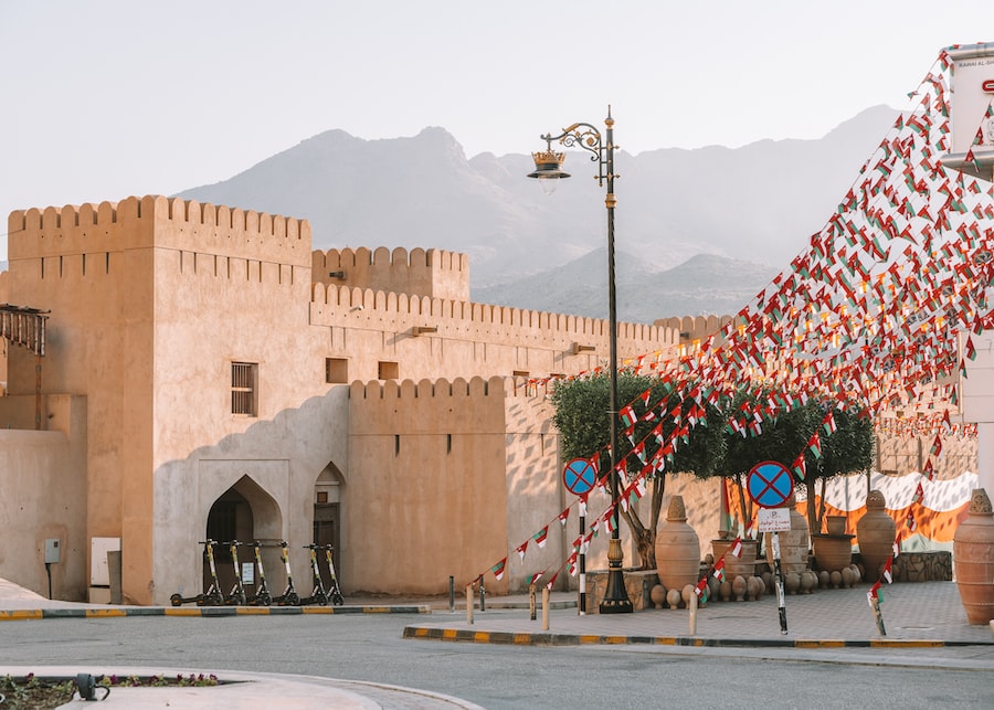 Outside view of the Nizwa Fort with streamers of Omani flags out front - one of the top spots to visit on an Oman road trip itinerary