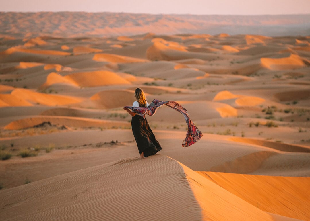 Michelle Halpern on the Wahiba Sands dunes at sunset holding a scarf along her Oman road trip itinerary