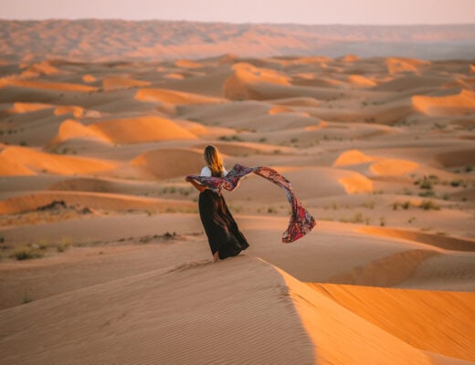 Michelle Halpern on the Wahiba Sands dunes at sunset holding a scarf along her Oman road trip itinerary