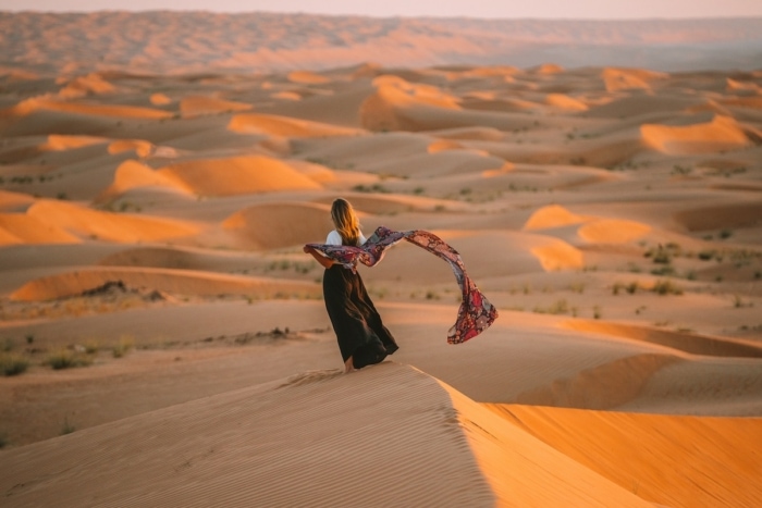 Michelle Halpern on the Wahiba Sands dunes at sunset holding a scarf along her Oman road trip itinerary