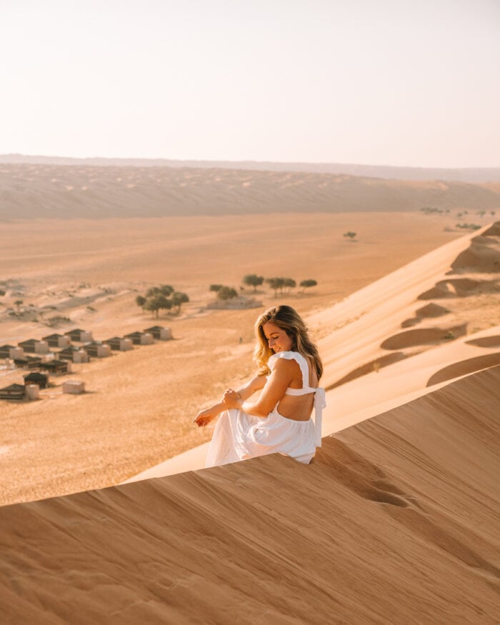 Michelle Halpern sitting on a dune overlooking 1000 Desert Nights on her Oman road trip itinerary