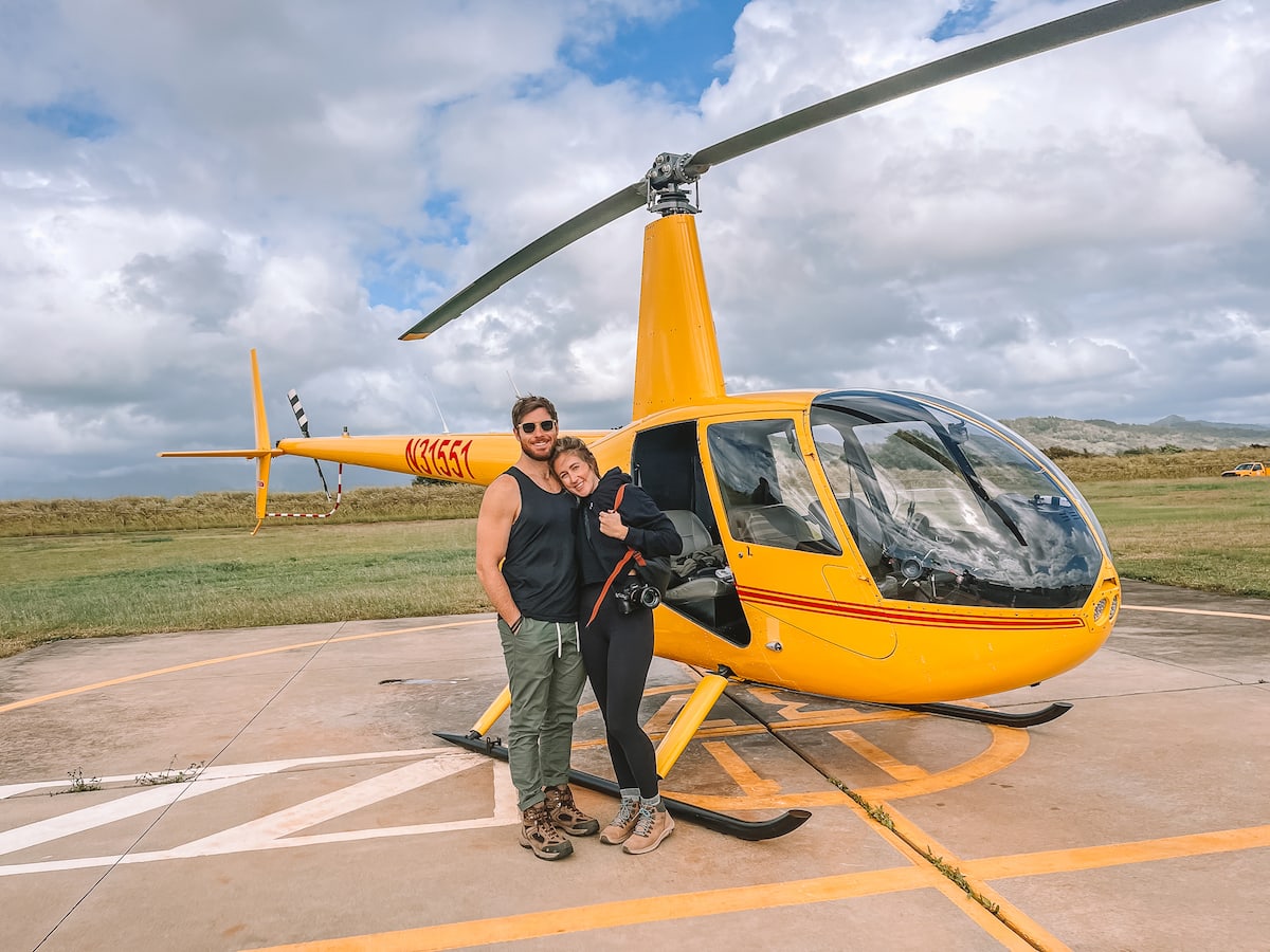 Couple standing outside a yellow helicopter in Kauai