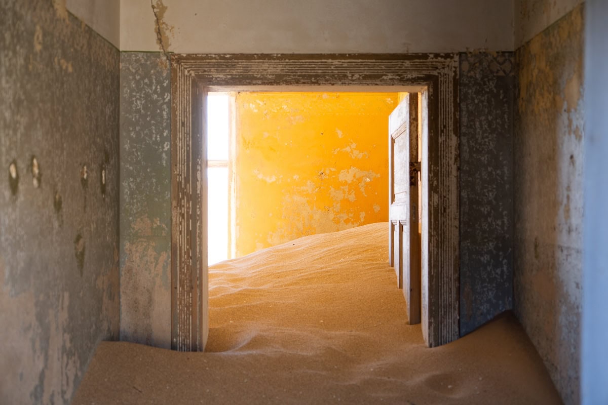 v guide Doorway surrounded by green paint at Kolmanskop Namibia with about a foot of sand covering the floor.