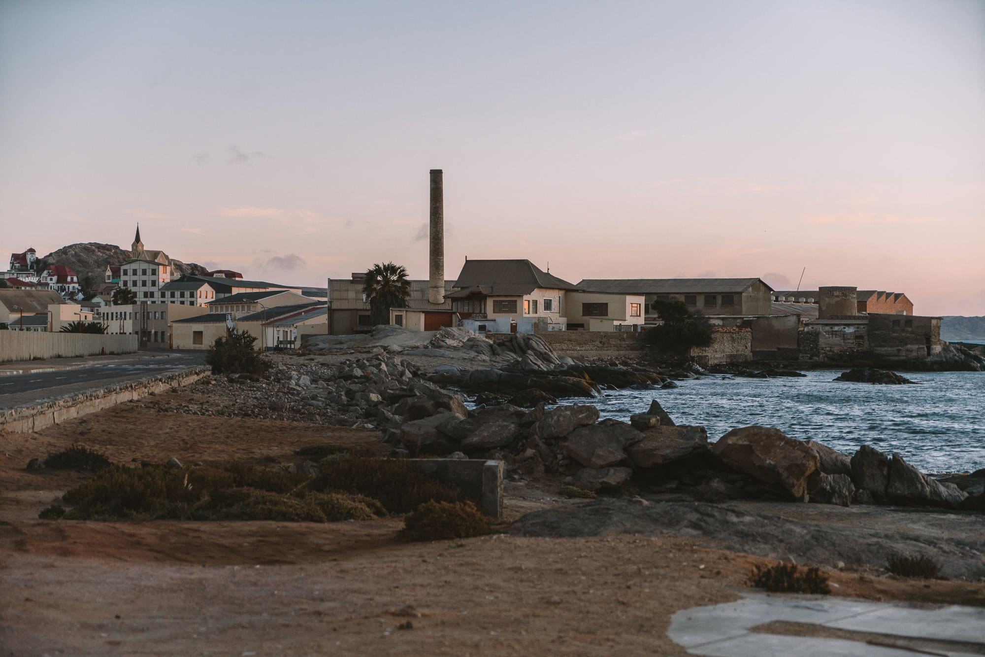 Coastline Coastline with ocean waves that leads to old buildings at sunset.