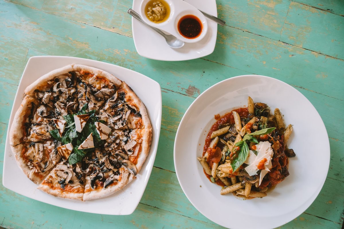 Top down view of two plates set against a turqouise table. One has pizza on it and the other pasta.