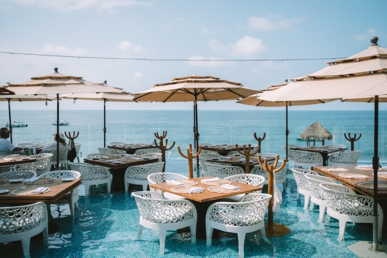View of restaurant tables at Mar y Vino that feature white chairs sitting inside a pool and topped with covered umbrellas.