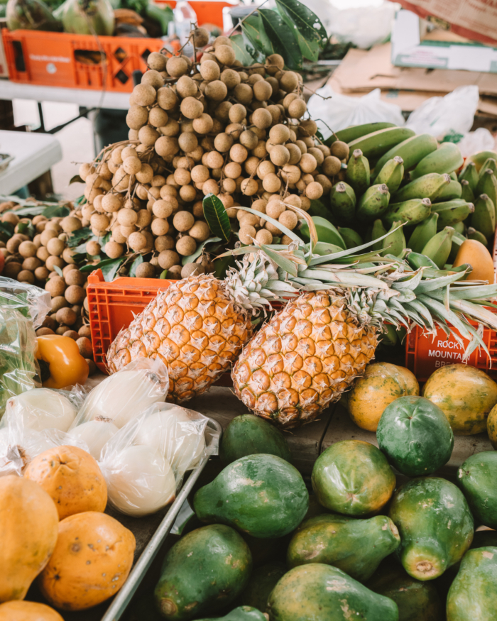tropical fruits market stand Colorful assortment of tropical fruits at a market stand. The image features pineapples, avocados, bananas and longan. They are displayed in crates and baskets.