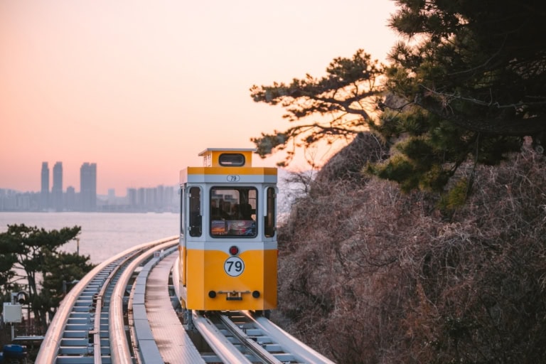 Capsule number 79, painted in sunshine yellow, cruises along the scenic seaside track during golden hour, capturing the charm of Busan’s iconic Sky Capsule ride.