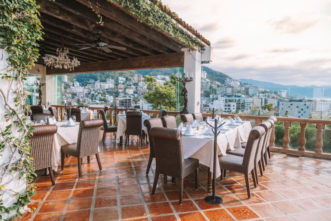 Fancy tables with white tablecloths on a rooftop patio overlooking the city of Puerto Vallarta