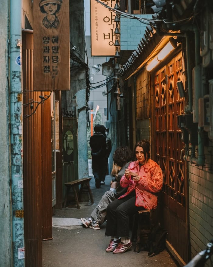 Jessica sits in an alleyway in Seoul drinking a coffee