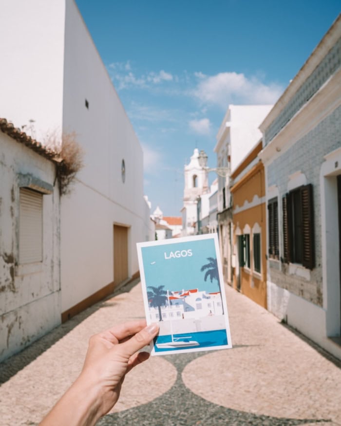 street in Lagos Hand holds up a Lagos postcard in front of a quaint street in Lagos, Portugal