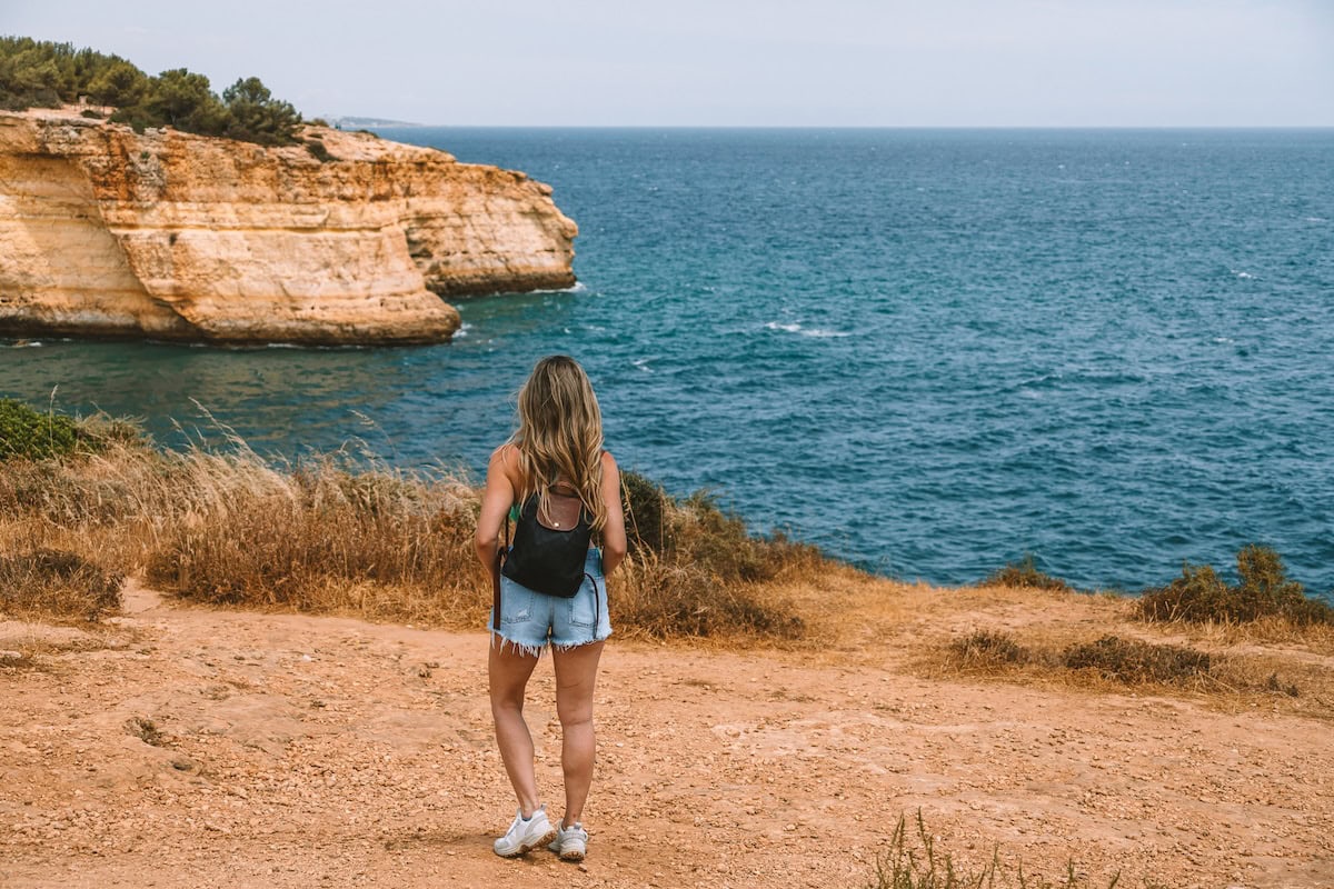 Seven Hanging Valley Trail Michelle Halpern standing with a backpack and jean shorts and sneakers on a dirt trail looking out on ocean