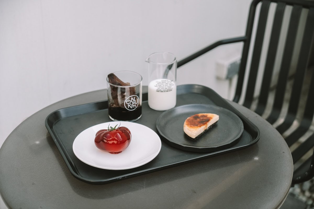 Nudake seoul Black round table with a tray on top that's full of two desserts, an iced coffee and glass of milk.