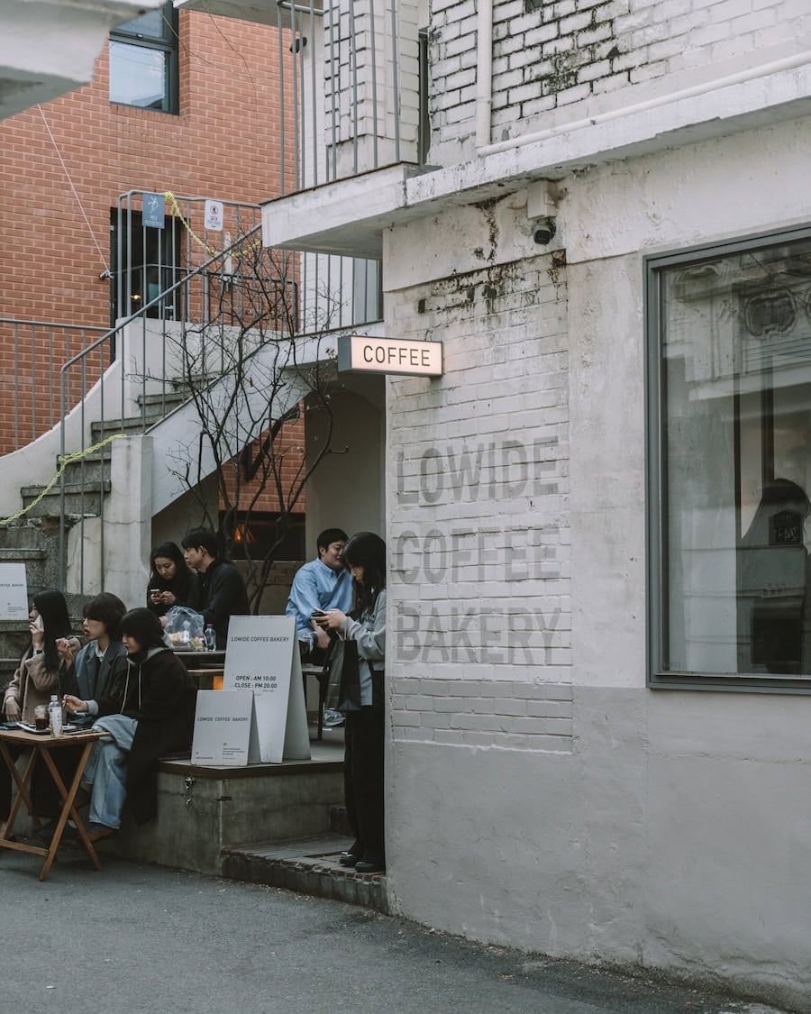 Lowide Coffee Bakery Exterior of gray and white brick building that reads "Lowide Coffee Bakery" in gray paint on the side and people sitting outside socializing