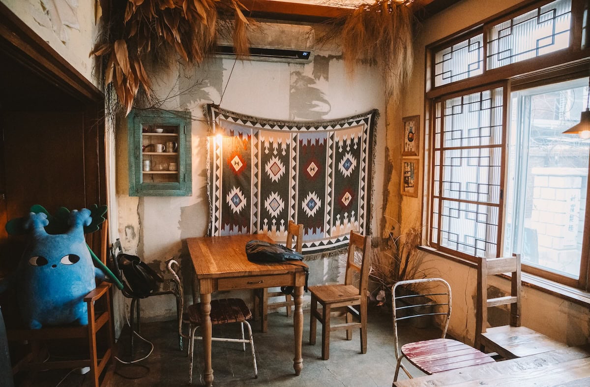 Cafe Dotori Garden Interior of a room at Dotori Garden cafe, one of the best cafes in Seoul - it's got wooden tables, a Ghibli character in the corner and a patterned tapestry hanging on the wall.