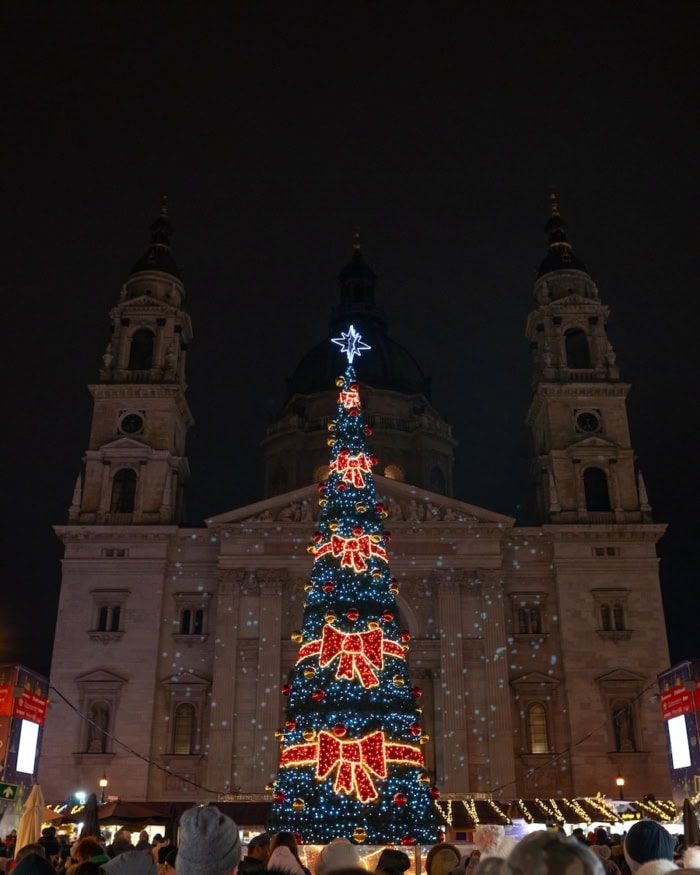 St Stephen's Basilica St Stephen's Basilica in Budapest at night lit up with festive projections and a large Christmas tree in front of it.