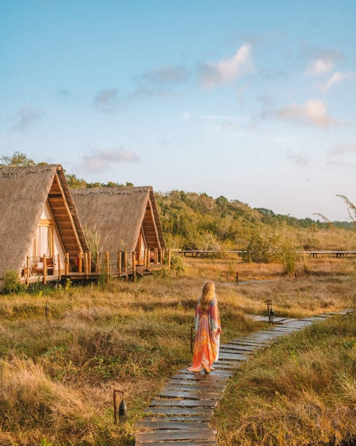Michelle Halpern standing on a wooden path with two lagoon facing rooms to her left