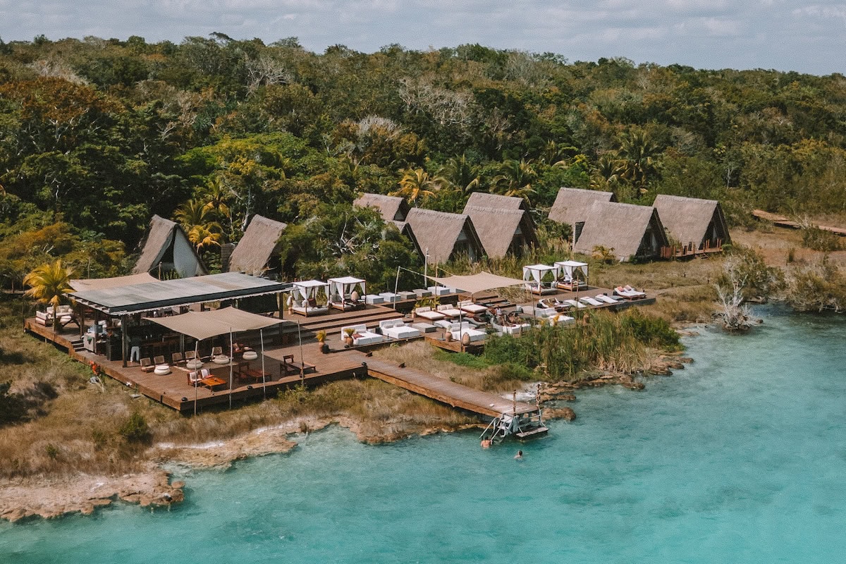 Drone shot of the Habitas Bacalar hotel property from above sitting right next to a turquoise lagoon