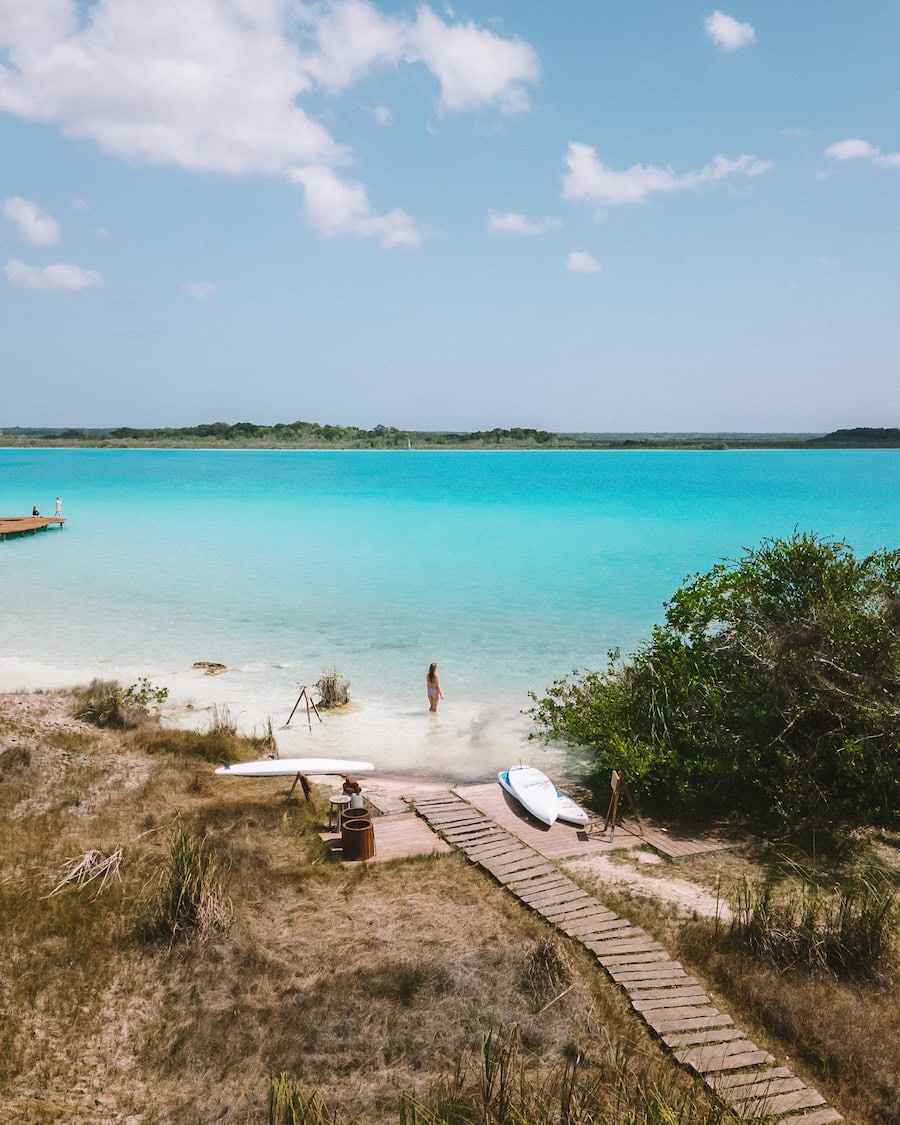 Michelle Halpern standing wading in Bacalar Lagoon with paddleboards at a nearby dock