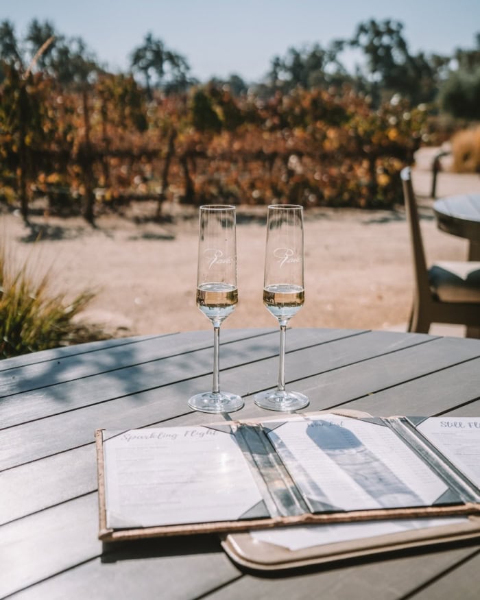 Rava Wines Two sparkling wine glasses sitting next to each other on a table with vineyards in the background
