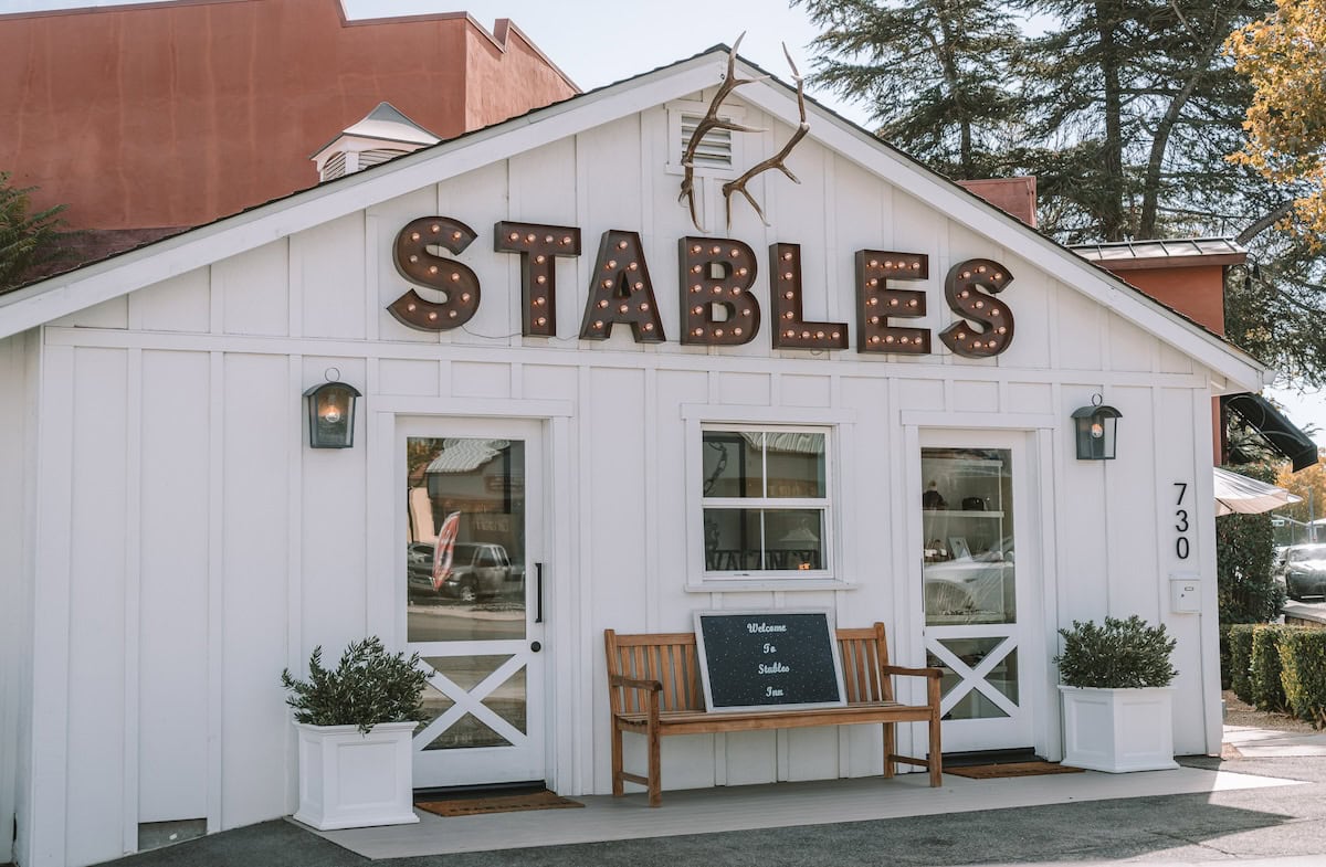 Stables white barn Exterior of the funky Stables in with a white barn feel, retro sign and bench out front.