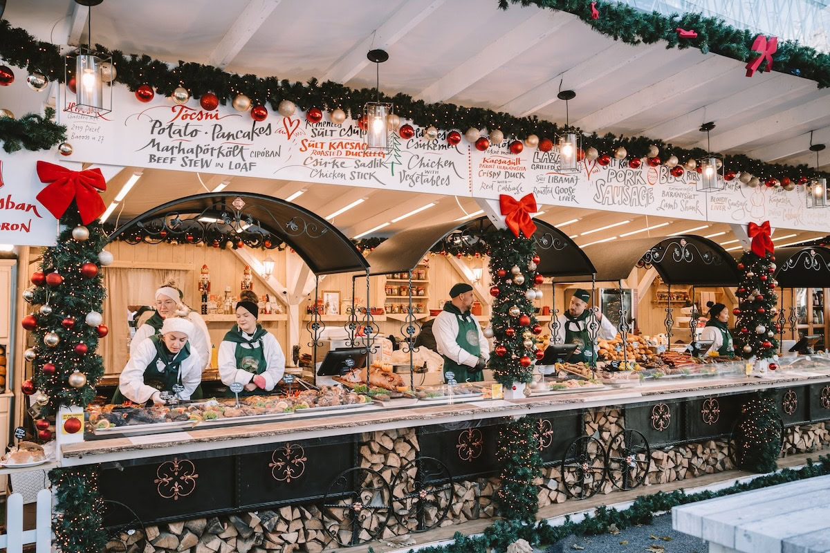 workers Vรถrรถsmarty Square Christmas Market Workers in white shirts and festive green vests standing behind the counters of food stalls at Vรถrรถsmarty Square Christmas Market