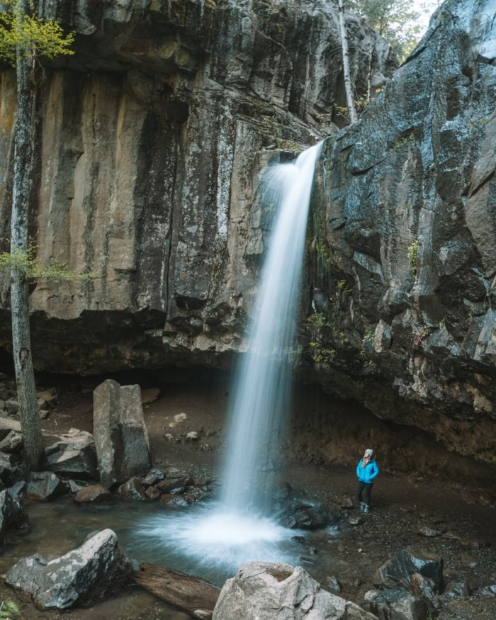 Hedge Creek Falls Michelle Halpern standing in a blue jacket behind Hedge Creek Falls, looking up at the waterfall