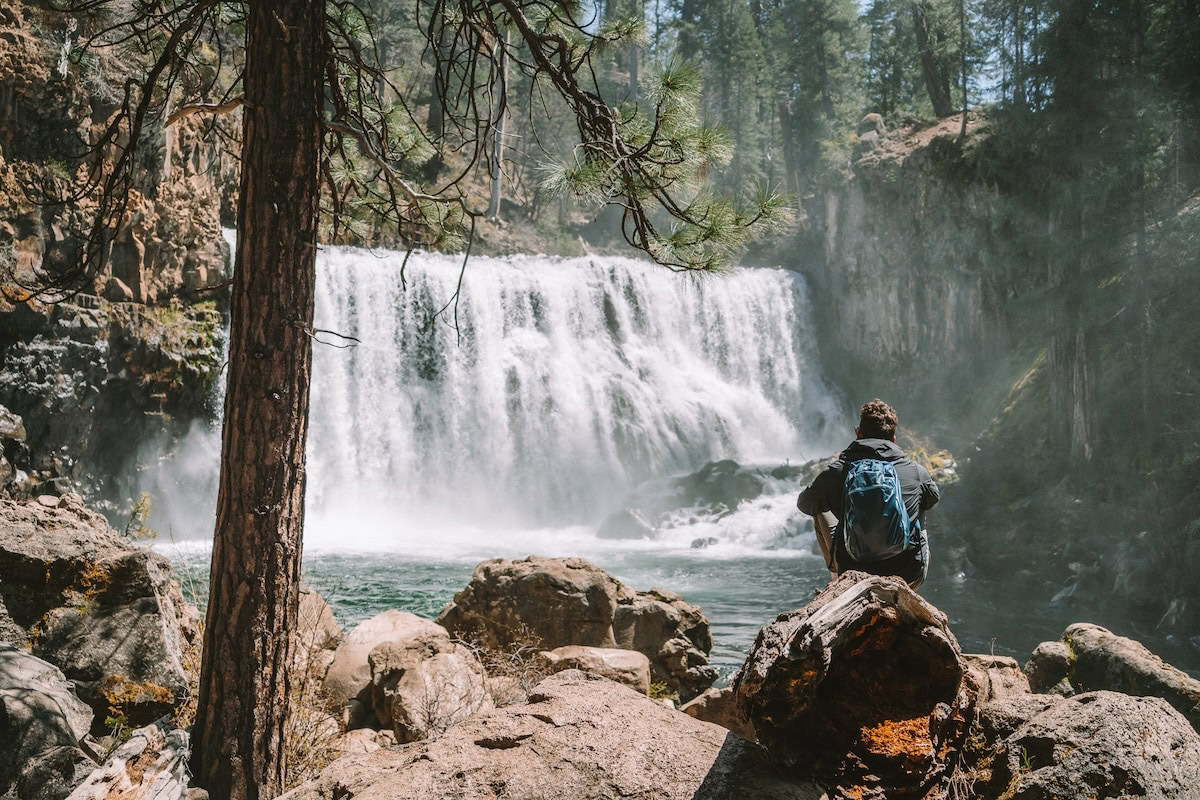 Middle Falls at McCloud Falls JT, Michelle's husband, sitting on a rock with a backpack on at the Middle Falls at McCloud Falls
