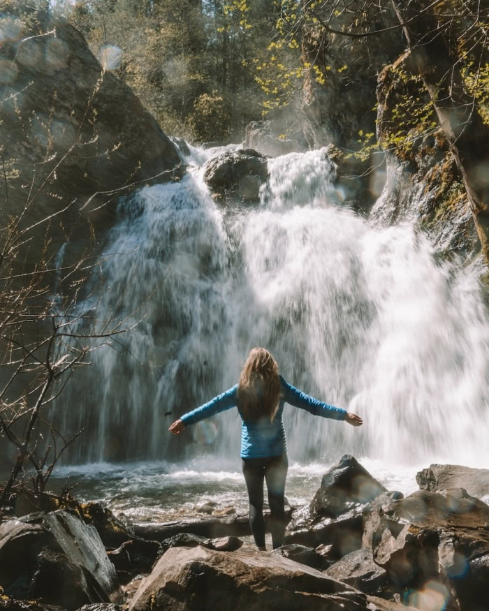 Faery Falls Michelle Halpern in blue puffy jacket standing on a rock in front of Faery Falls