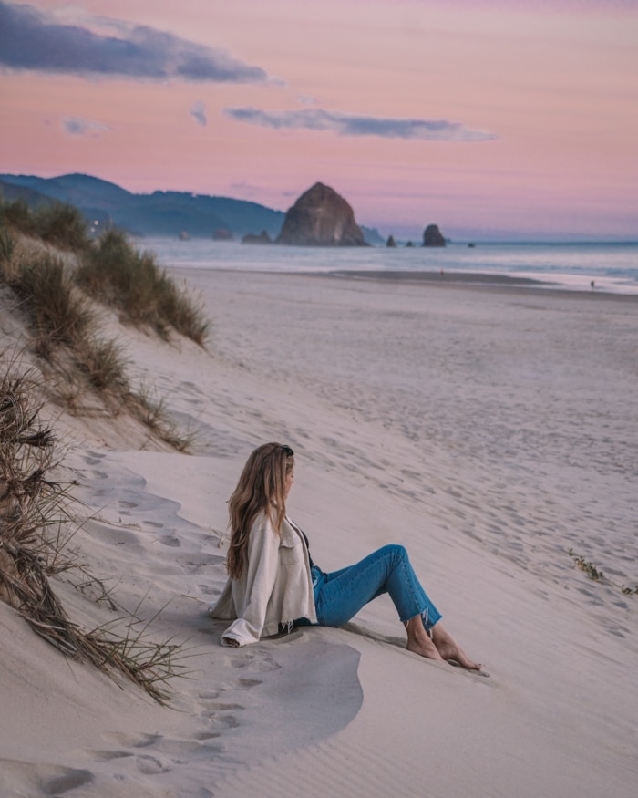 Best Oregon Coast Towns Michelle Halpern sitting on the sand at sunset in Cannon Beach, one of the Best Oregon Coast Towns