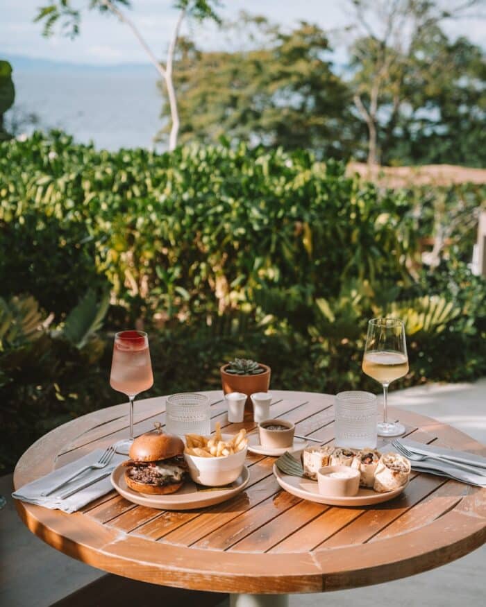 Outdoor table with two glasses of wine and burger and fries and a quesadilla