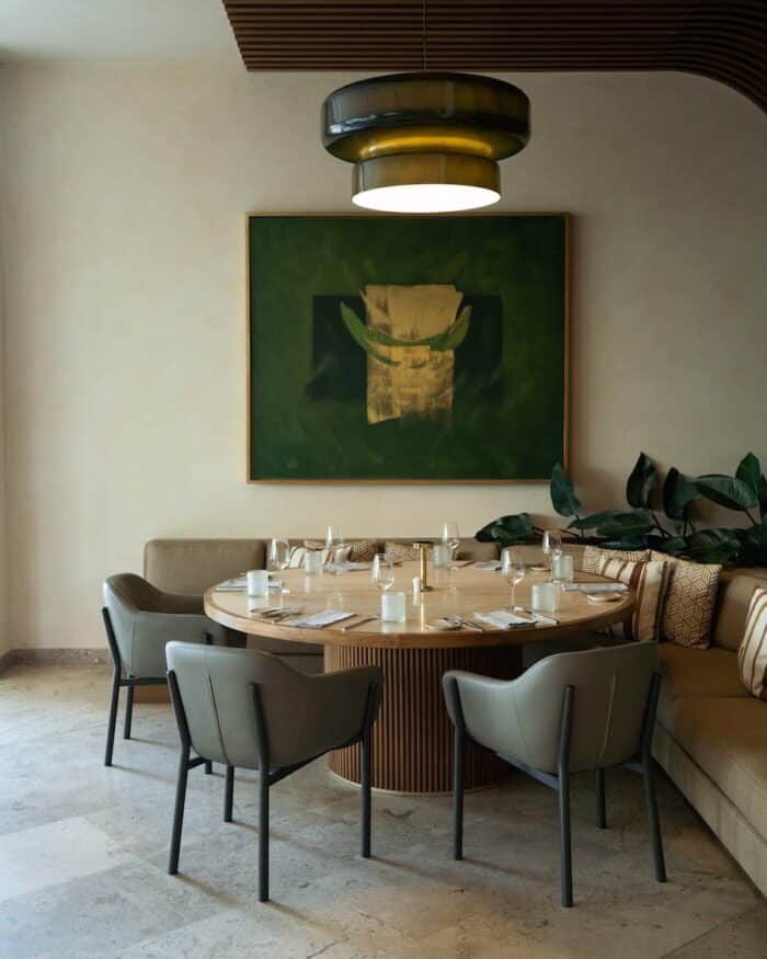 Interior design at Tico Tica featuring a big round table and chairs and a green painting on the wall.