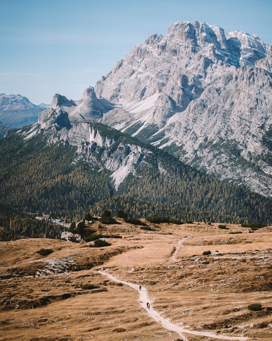 dramatic mountains and forest Tiny hikers walking along a trail with dramatic mountains and forest in the background