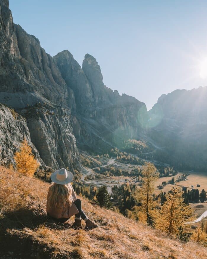 Michelle Halpern sitting on a grassy hill looking down over the winding roads of Gardena Pass