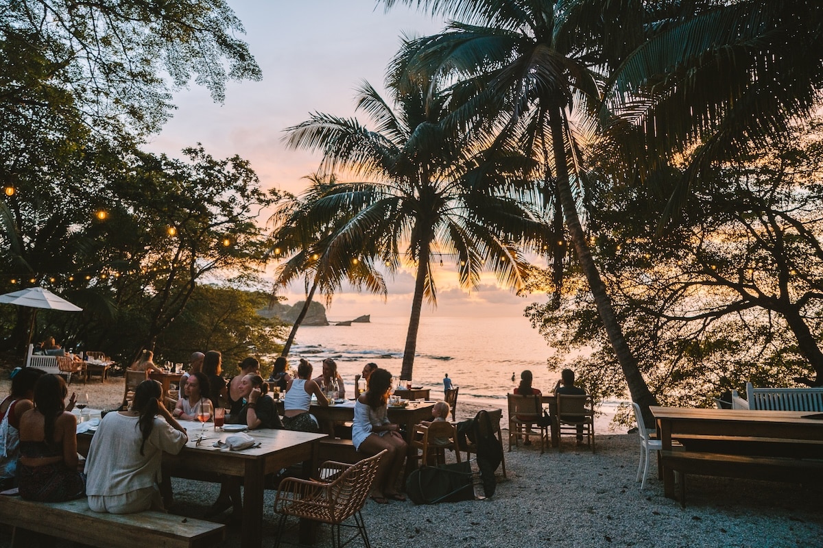 La Luna Restaurant People sitting at long wooden tables at a restaurant at sunset - La Luna Restaurant in Nosara, Costa Rica